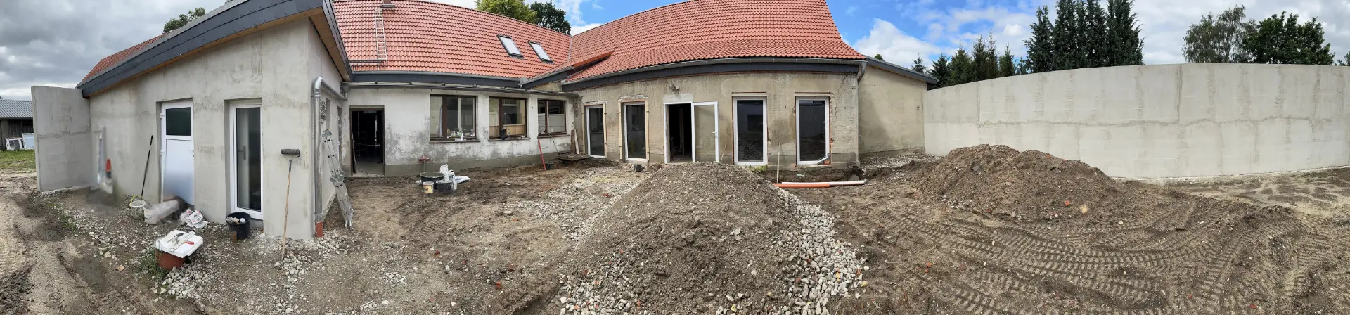 Panorama der Umbauphase im Hof von Friends: neue rote Ziegeldächer, verputzte Rohwände, neue Fenster und Türen, davor aufgeschütteter Sand und Schotter