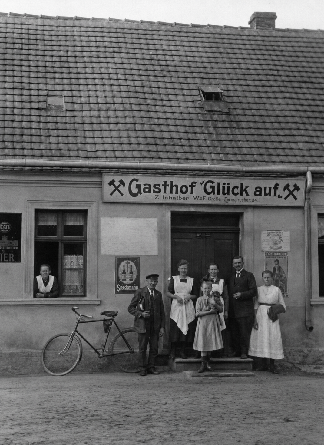 Historische Aufnahme des Gasthofs ‚Glück auf‘ in Bräsen: Wirtsleute und Kinder vor dem Eingang, darüber das Schild mit Fernsprecher 34