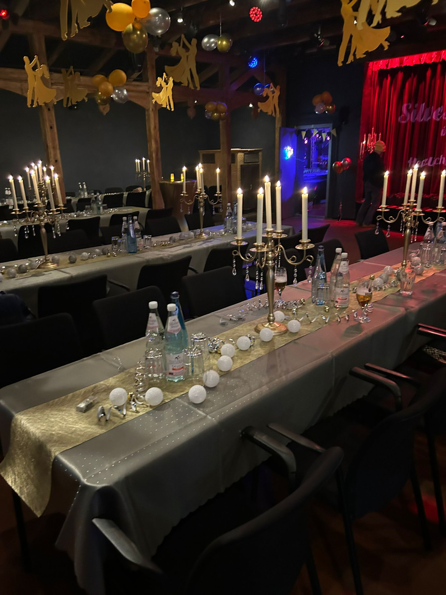 Lange Tafeln mit Kerzen und goldenen Tanzpaar-Silhouetten im Theatersaal zu Silvester
