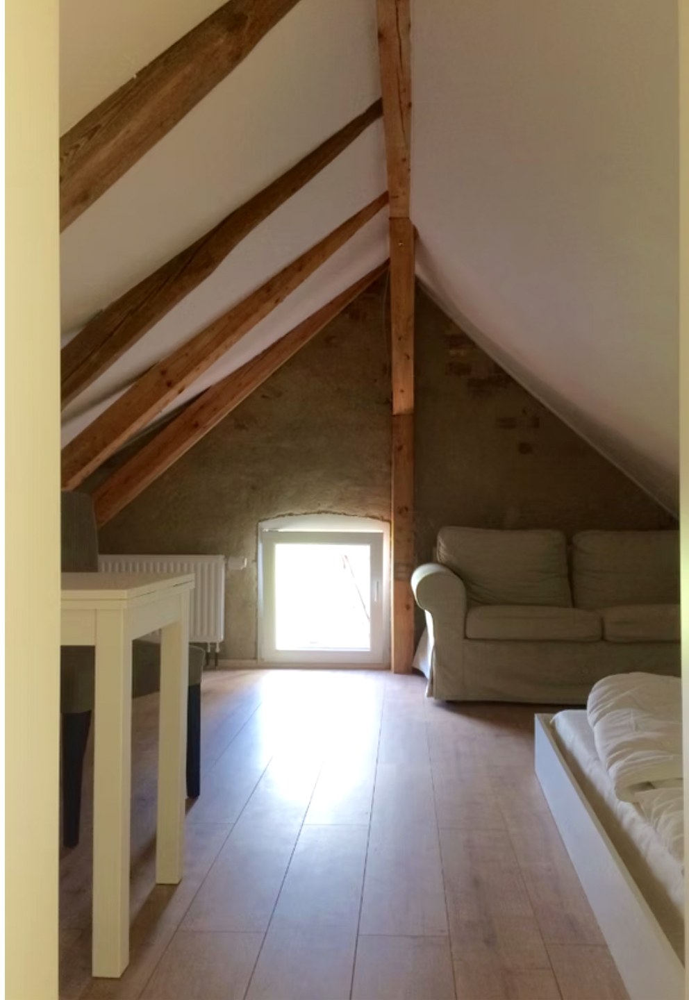 Zimmer unter dem Dach im Gästehaus: alte Holzbalken, Sofa, Tisch und Bett
