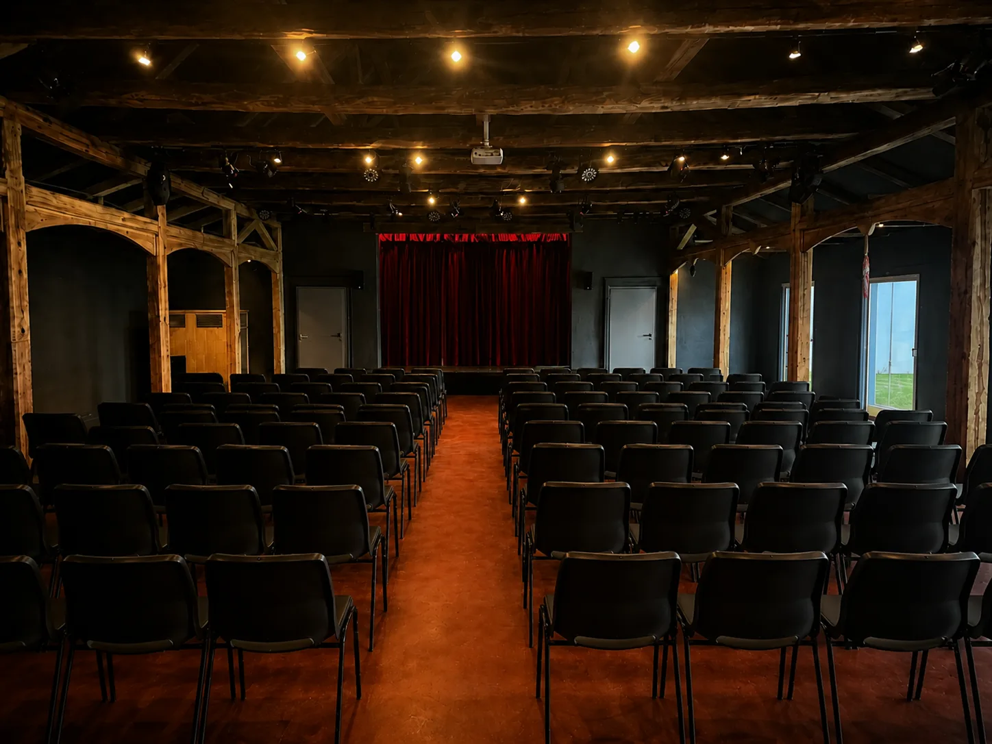 Bestuhlter Theatersaal mit rotem Bühnenvorhang und Holzbalken