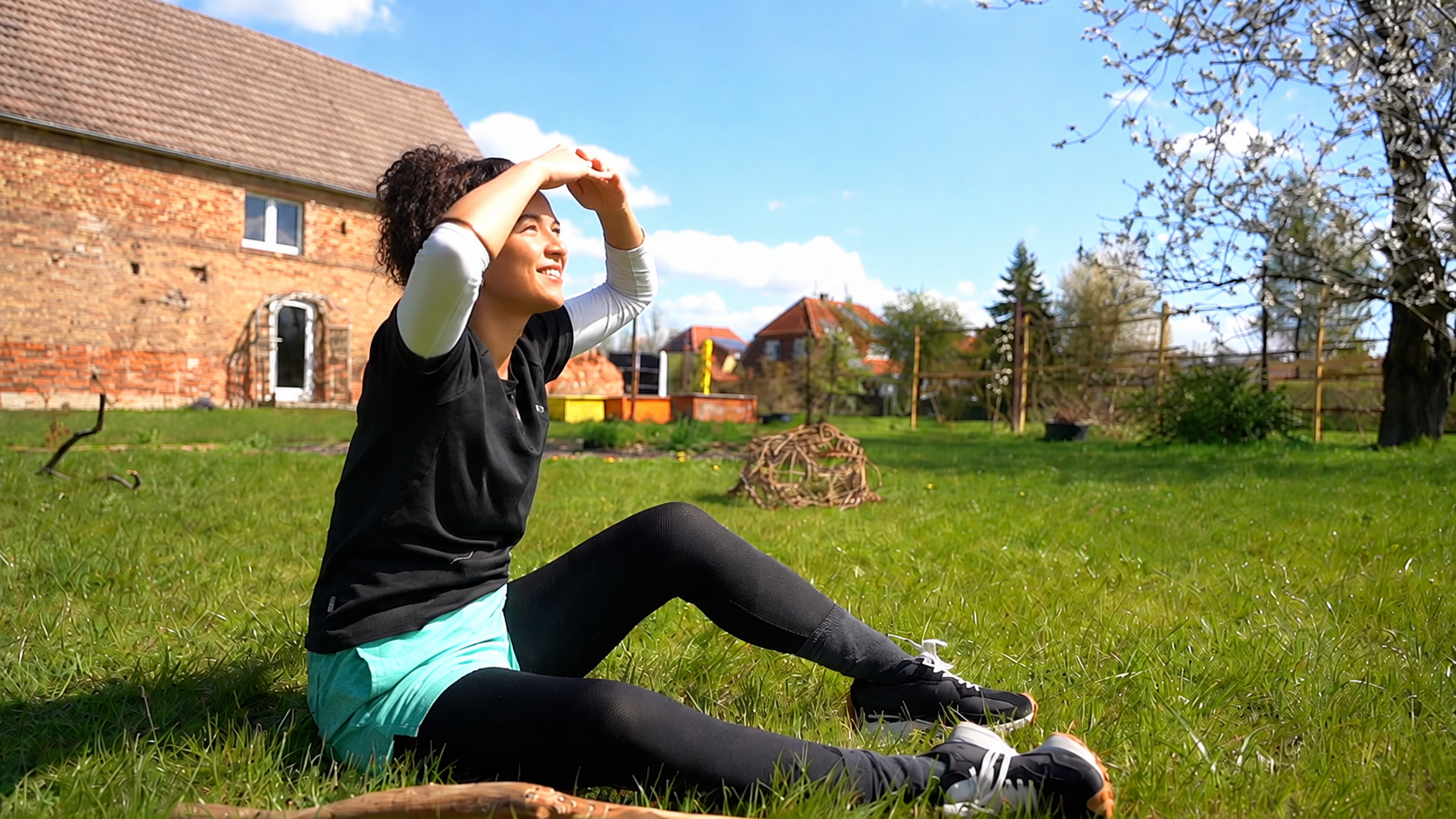 Frau sitzt in der Sonne auf der Wiese vor dem alten Klinkerstall