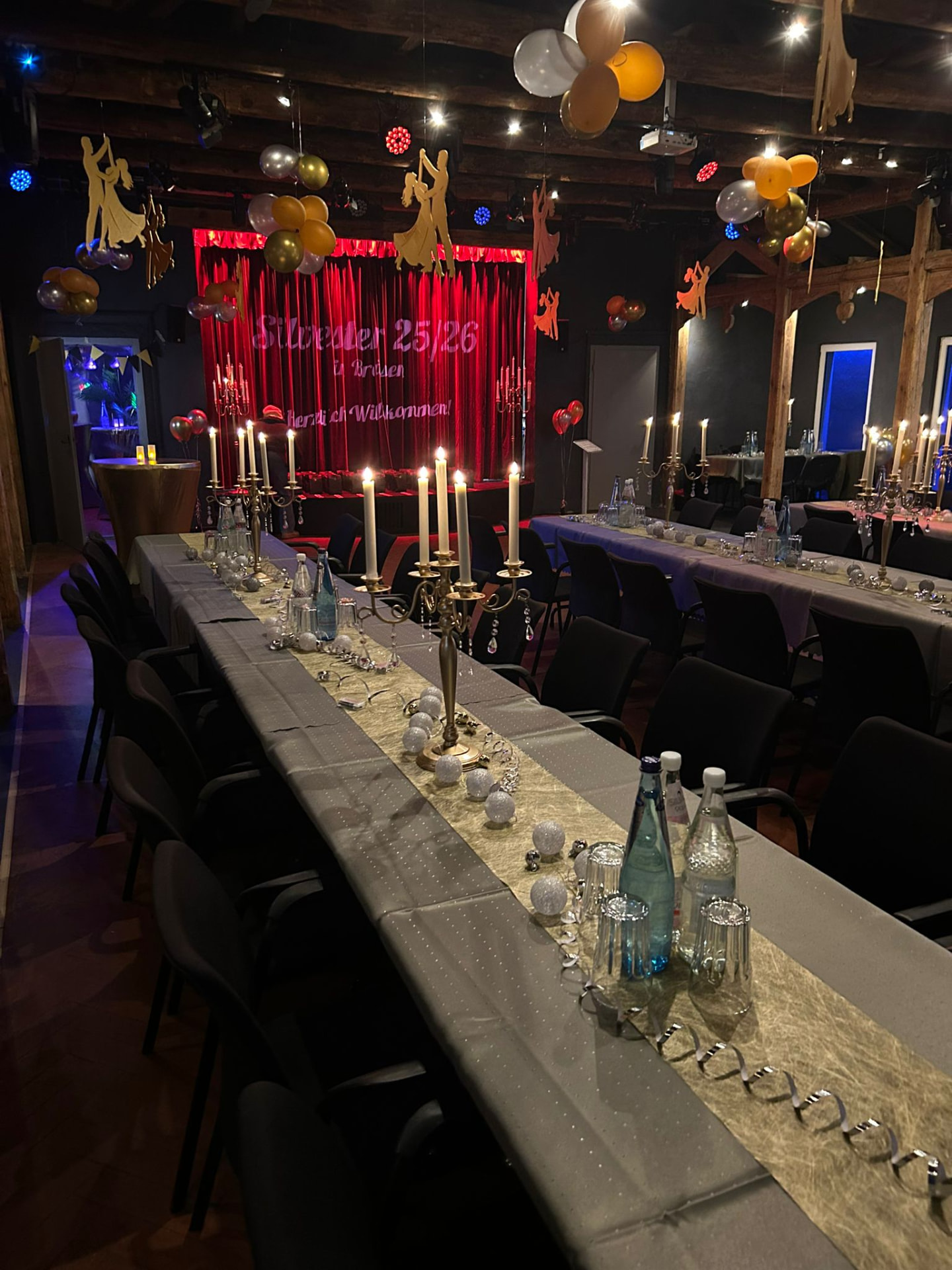 Festlich gedeckte Tafel mit Kerzenleuchtern vor der roten Silvesterbühne im Theatersaal