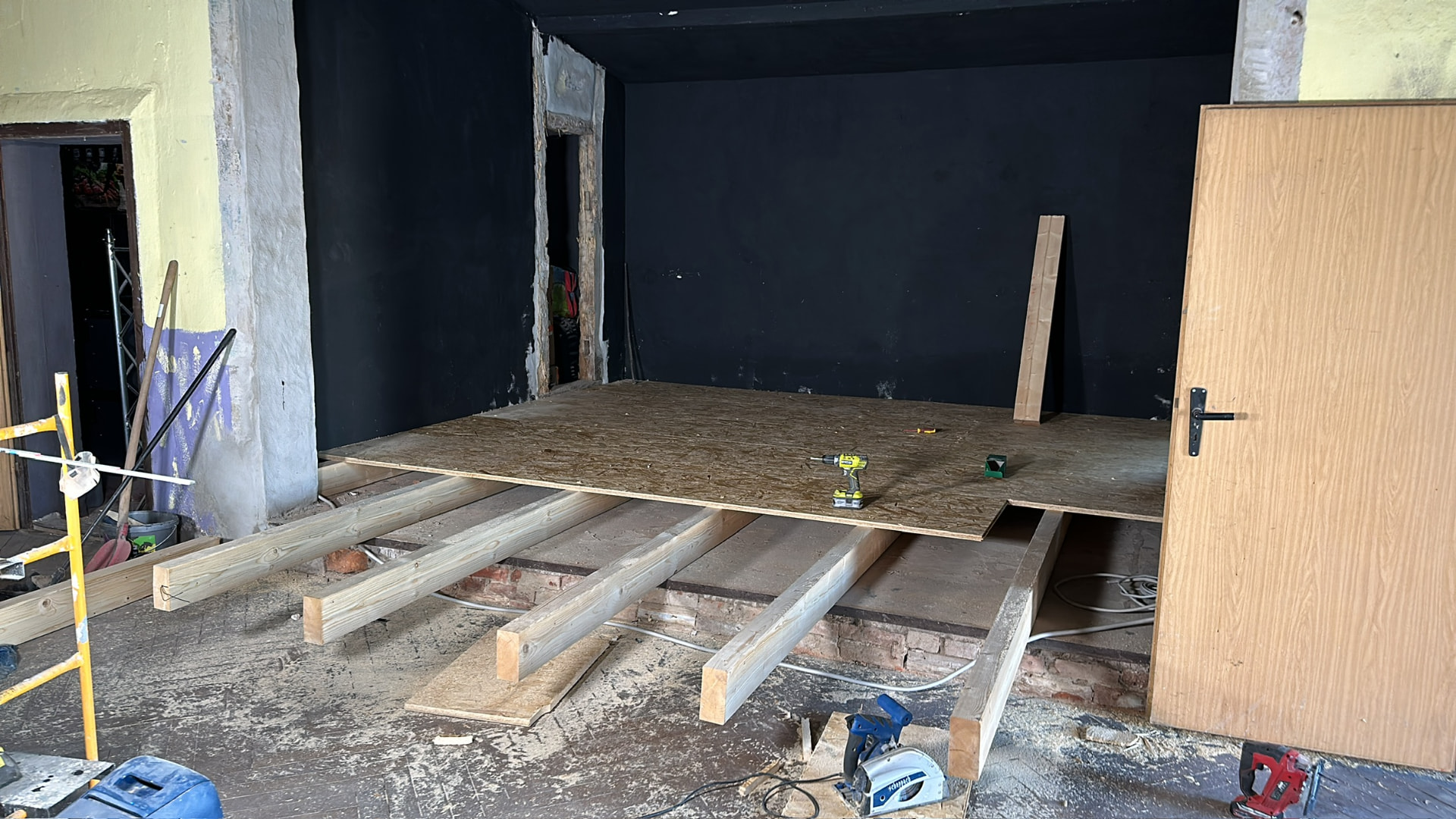 Bau der Bühne im Theatersaal von Friends: Holzbalken als Unterkonstruktion und erste OSB-Platten vor der schwarz gestrichenen Bühnenwand
