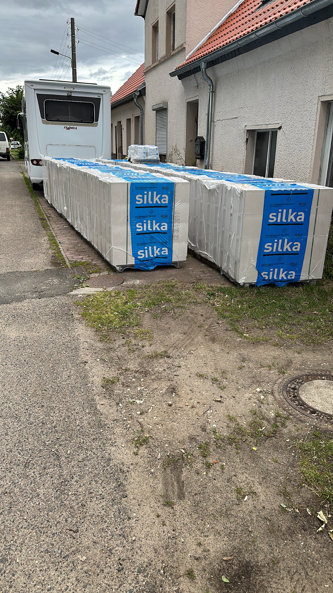 Anlieferung: Paletten mit Silka-Kalksandsteinen für den Biergarten stehen auf der Dorfstraße neben den Gebäuden von Friends