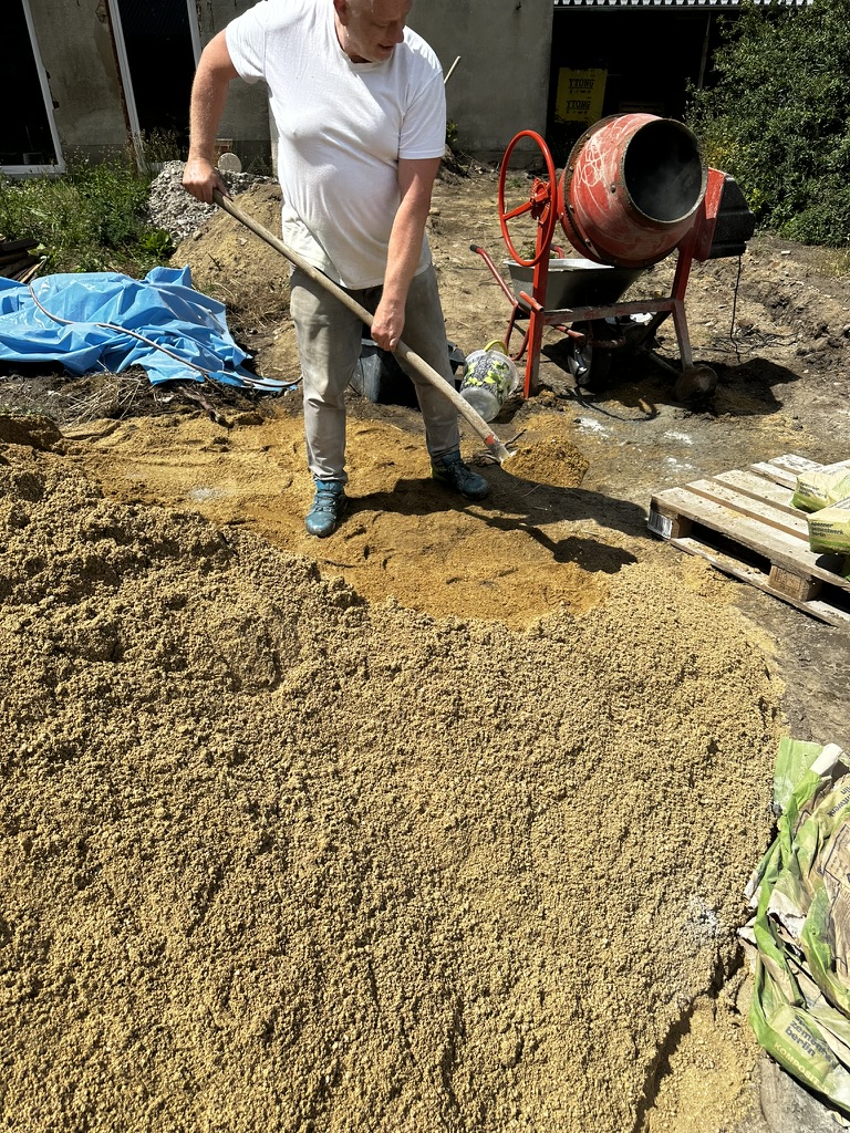 Steffen schaufelt Sand von Hand vor einem roten Betonmischer beim Bau des Fundaments für die Gartenmauer bei Friends