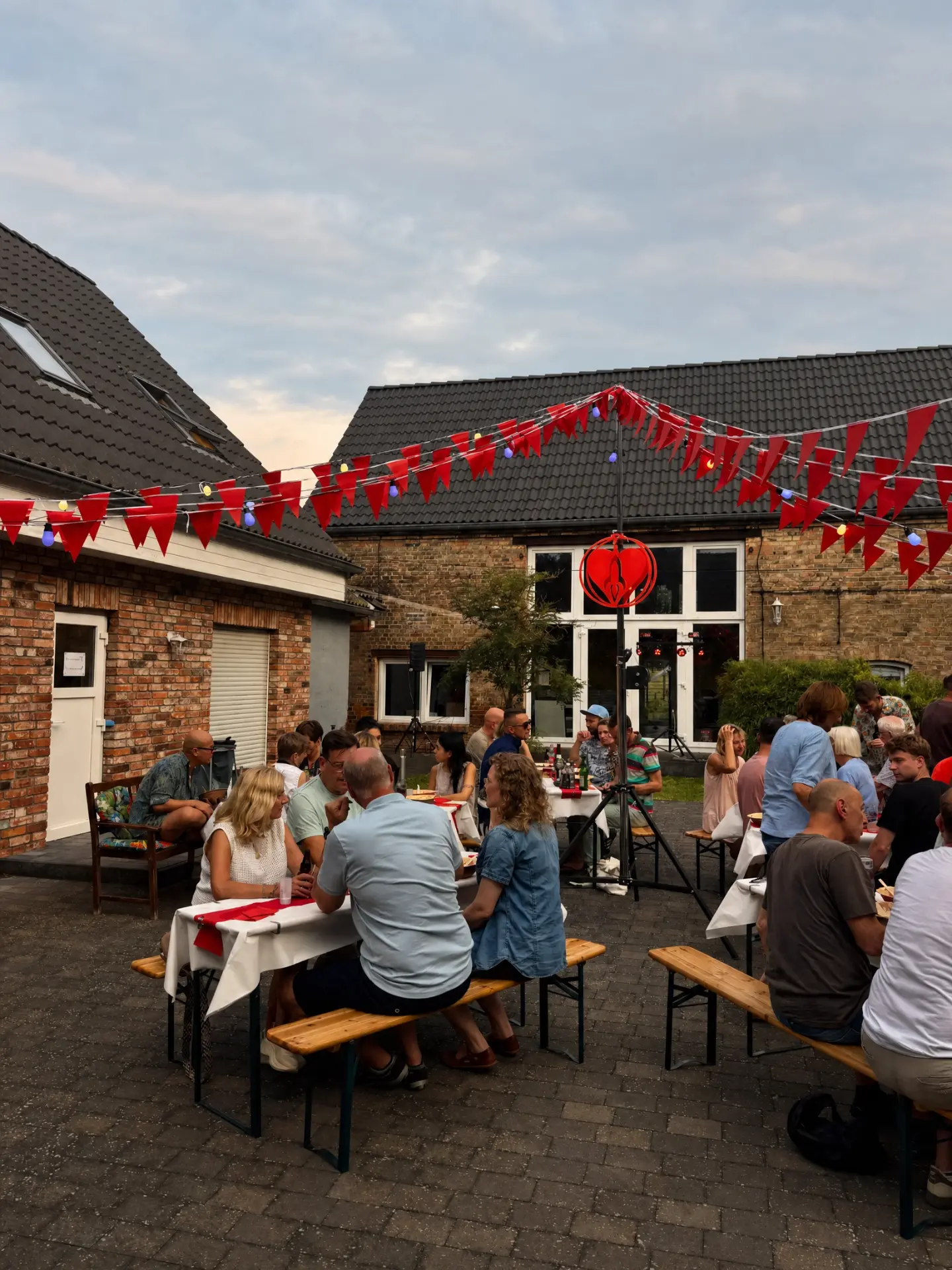 Lange Tafeln mit Bierbänken im Innenhof unter roten Girlanden